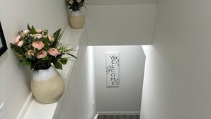 A staircase with a 'WELCOME' sign, white walls, and two vases with flowers. - Luxury 2 Bedroom Basement Suite in NW, Calgary (Calgary)