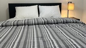 A bed with a striped bedspread, two white pillows, and a framed landscape photo above it. - Luxury 2 Bedroom Basement Suite in NW, Calgary (Calgary)
