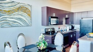 A modern kitchen with dark cabinets, a microwave, a stove, and a refrigerator. There is a dining table with chairs and a vase of flowers.