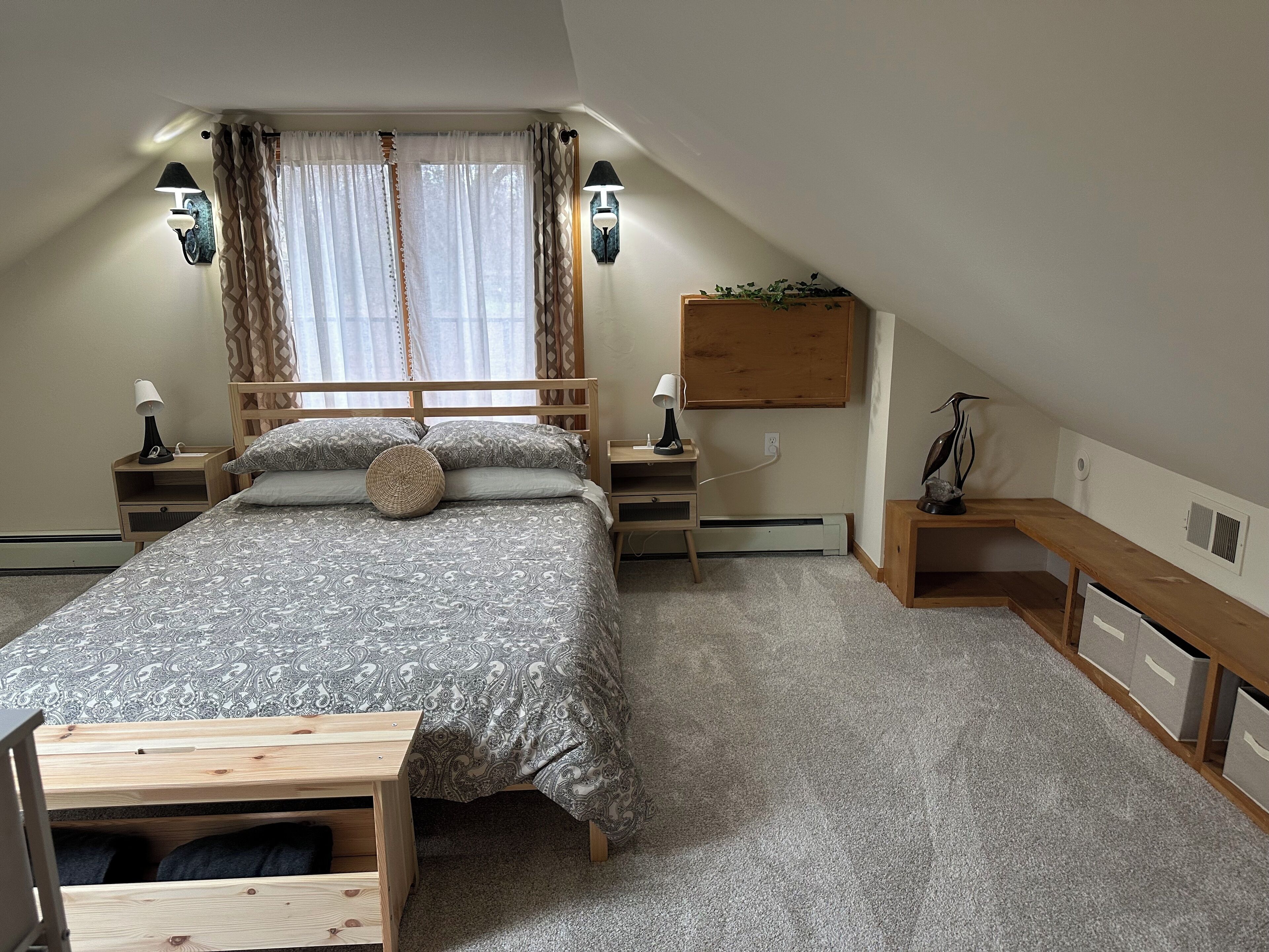 Une chambre à coucher comprenant un lit, des tables de chevet, un bureau, un banc et une fenêtre avec des rideaux.