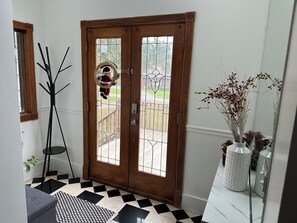 A wooden door with glass panels, a coat rack with a hat, a patterned rug, and a white vase with branches. - Charming 6-bedroom house in marvelous Rochester Hills with a fitness room, WiFi (Rochester Hills)