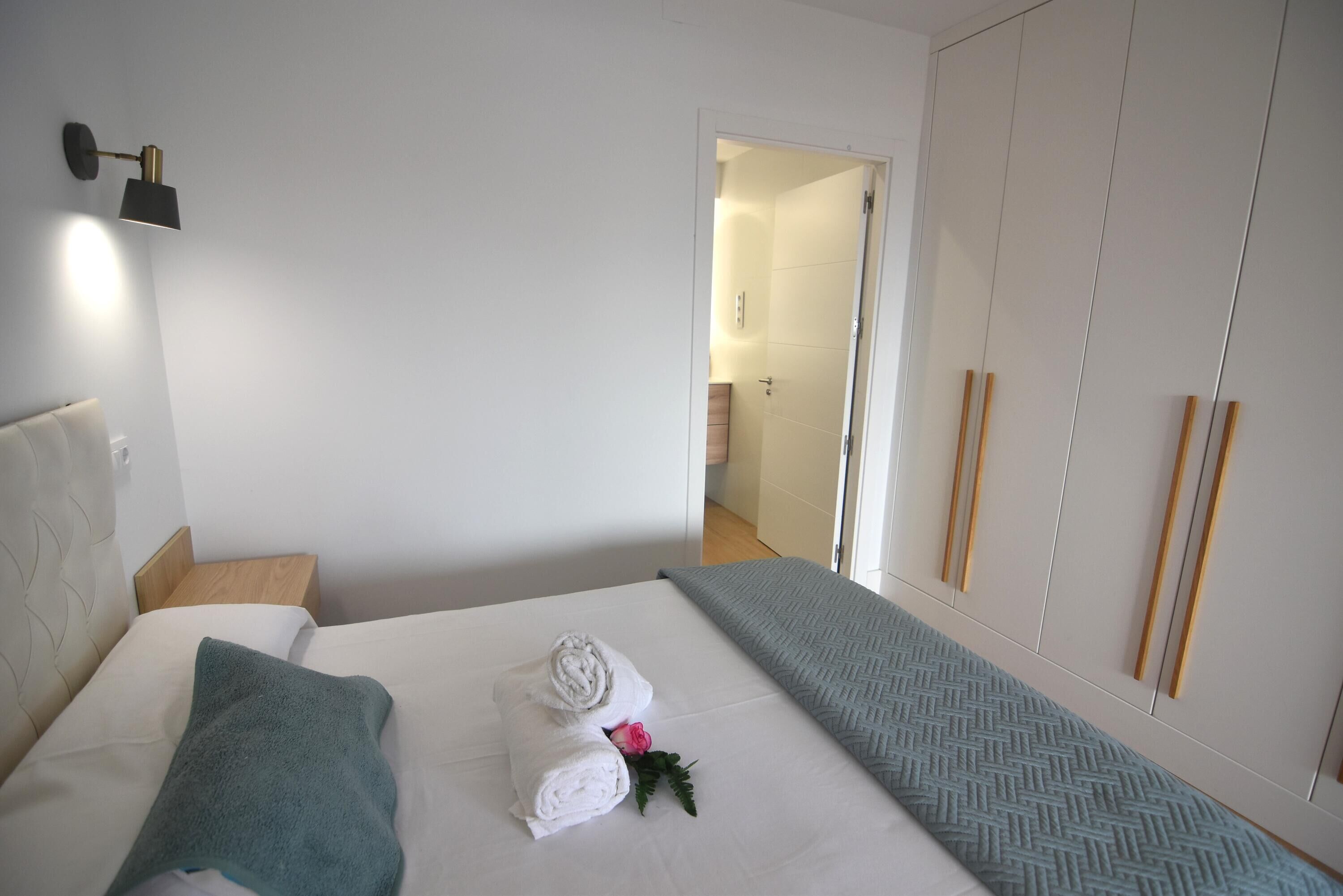 Een hotelkamer met een bed, nachtkastje, wandlamp en kledingkast.