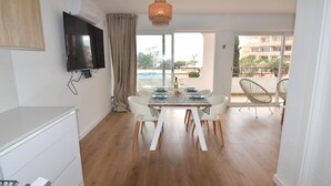 Un comedor moderno con una mesa de madera dispuesta para cuatro personas, sillas blancas y un televisor montado en la pared.