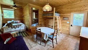 Interior acogedor de una cabaña con cama, una mesa de comedor con sillas, una escalera y una puerta de madera con un letrero.