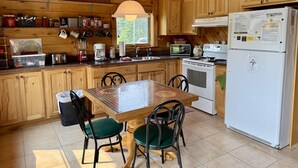Cocina de cabaña de madera con una mesa de comedor, sillas, un refrigerador y varios electrodomésticos.