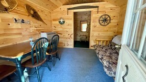Interior de una cabaña de madera con una mesa de comedor, sillas, un sofá, decoración de pared con una brújula y una ventana pequeña.