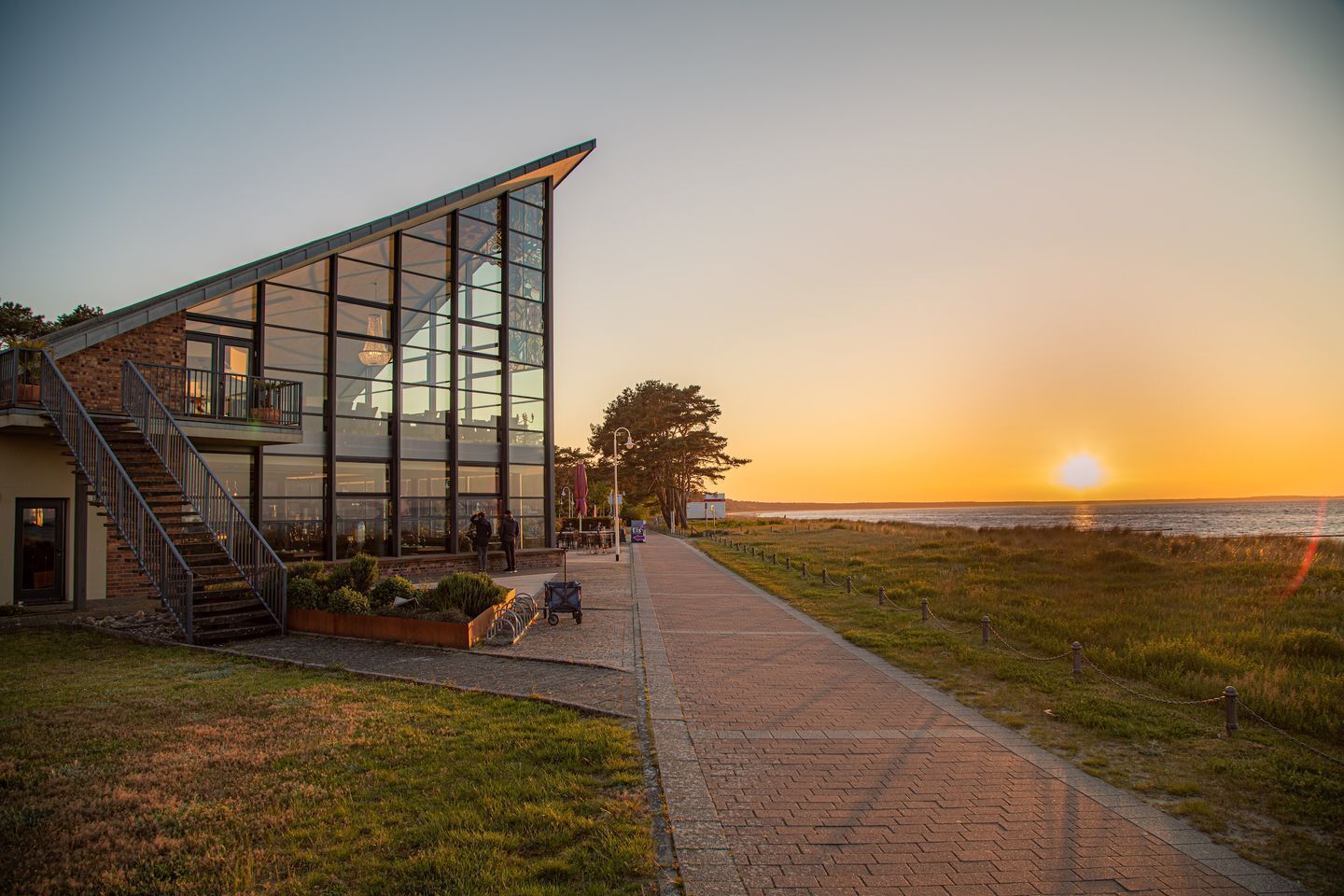 Een modern gebouw met grote glasramen, een trap en een pad naar het strand.