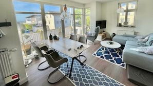 A modern living room with a dining area, large windows, and a view of the city. - Vacation apartment Meehr Glowe - Villa Rosa - Holiday apartment Mee(h)r (Glowe)