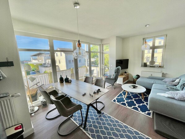 A modern living room with a dining area, large windows, and a view of the city.