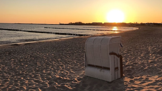 A beach with a white wicker chair in the foreground and a sunset in the background. - Vacation apartment Meehr Glowe - Villa Rosa - Holiday apartment Mee(h)r (Glowe)