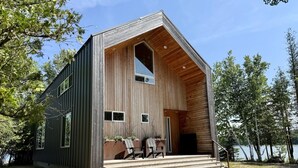 Una cabaña moderna con techo inclinado, ventanas grandes y fachada de madera.
