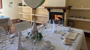 Een eettafel gedekt voor een maaltijd, compleet met wijnglazen, borden en bestek. Een witte ballon is aan de tafel vastgemaakt, en in de achtergrond is een open haard te zien.