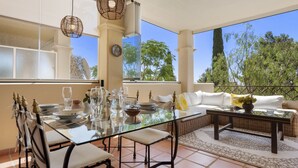 A dining area with a glass table, white chairs, and a sofa with yellow cushions. - Sunny Terrace Apt in Golf Valley with Pool (Estepona)