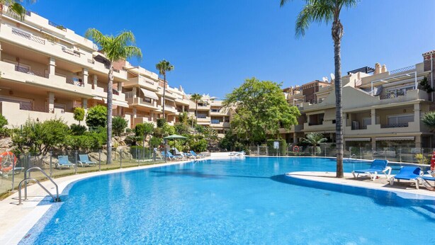 A swimming pool with lounge chairs, palm trees, and multi-story buildings in the background. - Sunny Terrace Apt in Golf Valley with Pool (Estepona)
