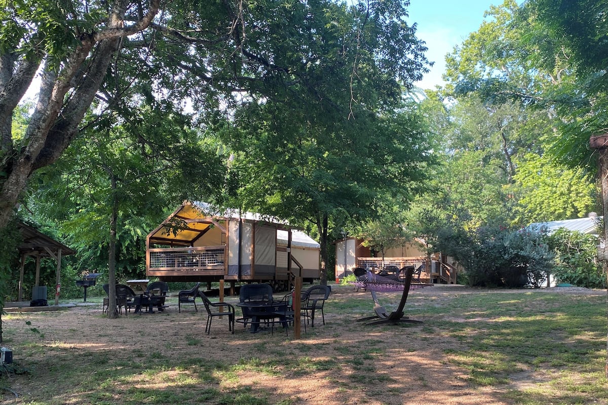 A rustic outdoor area with a wooden structure, tables, chairs, and a hammock.