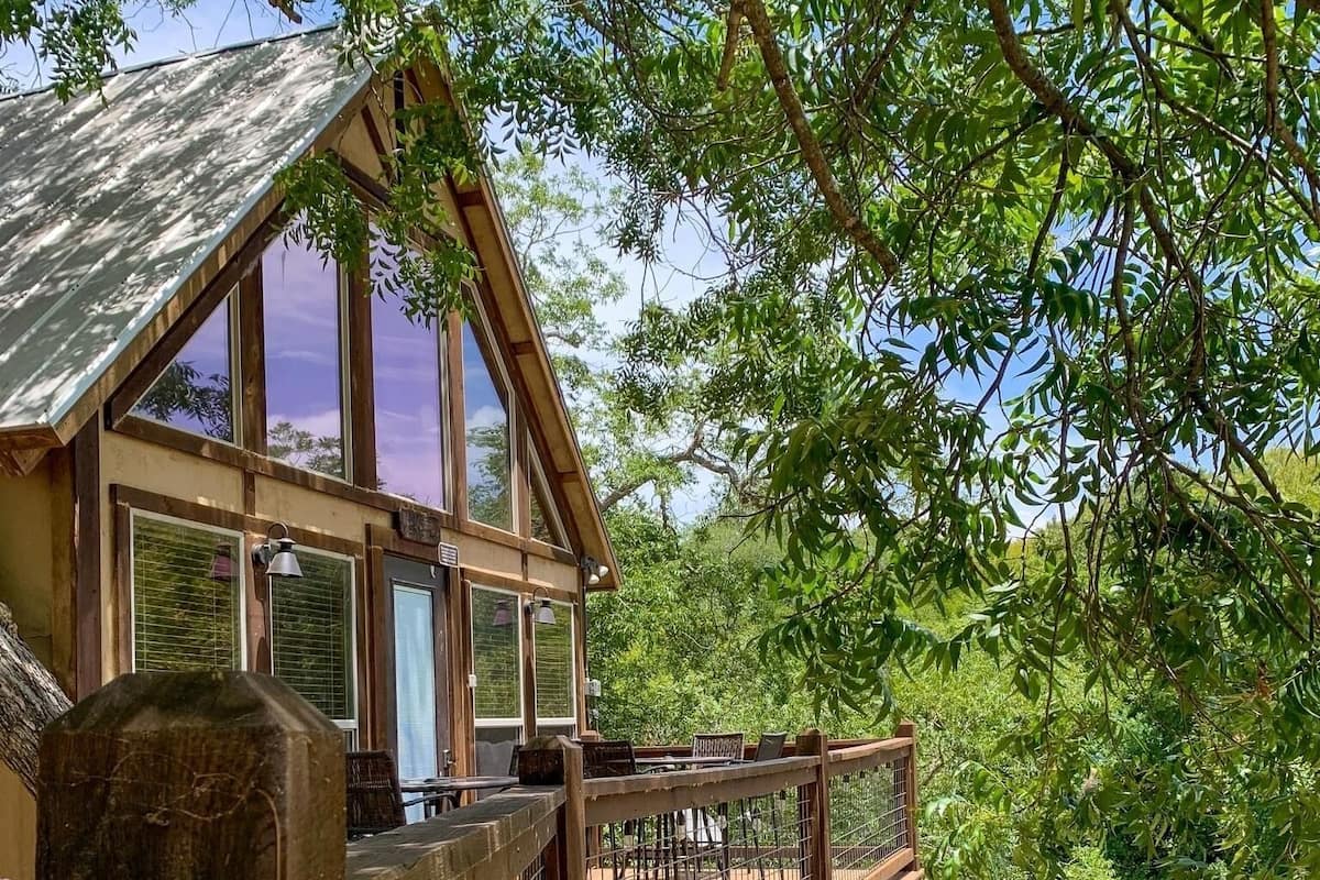 A wooden cabin with a balcony overlooking a green body of water, surrounded by trees.
