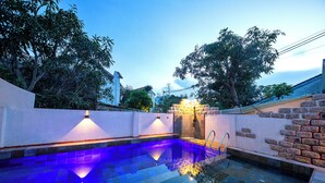 Una piscina con una fuente de agua azul cristalina, rodeada por un muro de piedra y una cerca blanca.