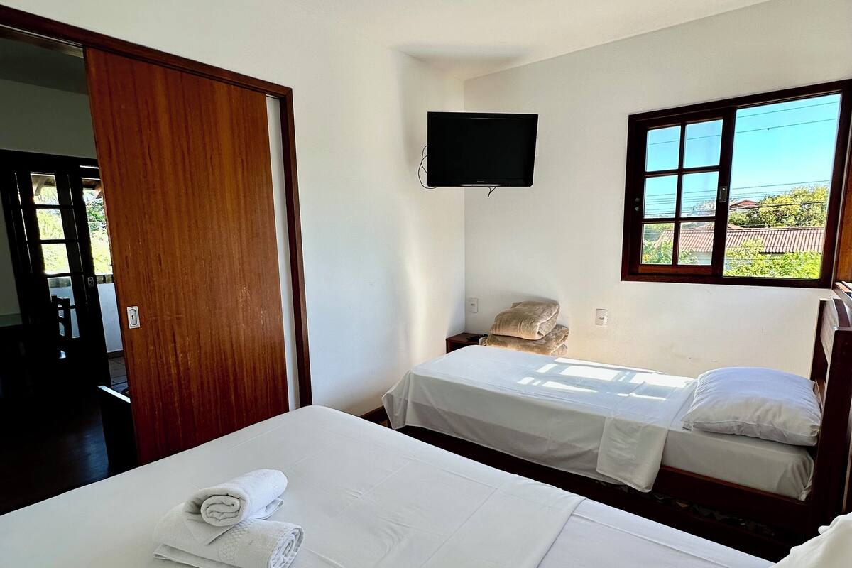 Ein Hotelzimmer mit zwei Betten, einem an der Wand montierten Fernseher und einem Fenster mit Blick auf Grünflächen.