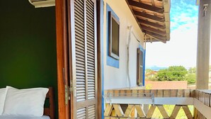 A room with a bed, a wooden door, a small trash bin, and a view of the outside. - Pousada Natur Campeche (Florianópolis)