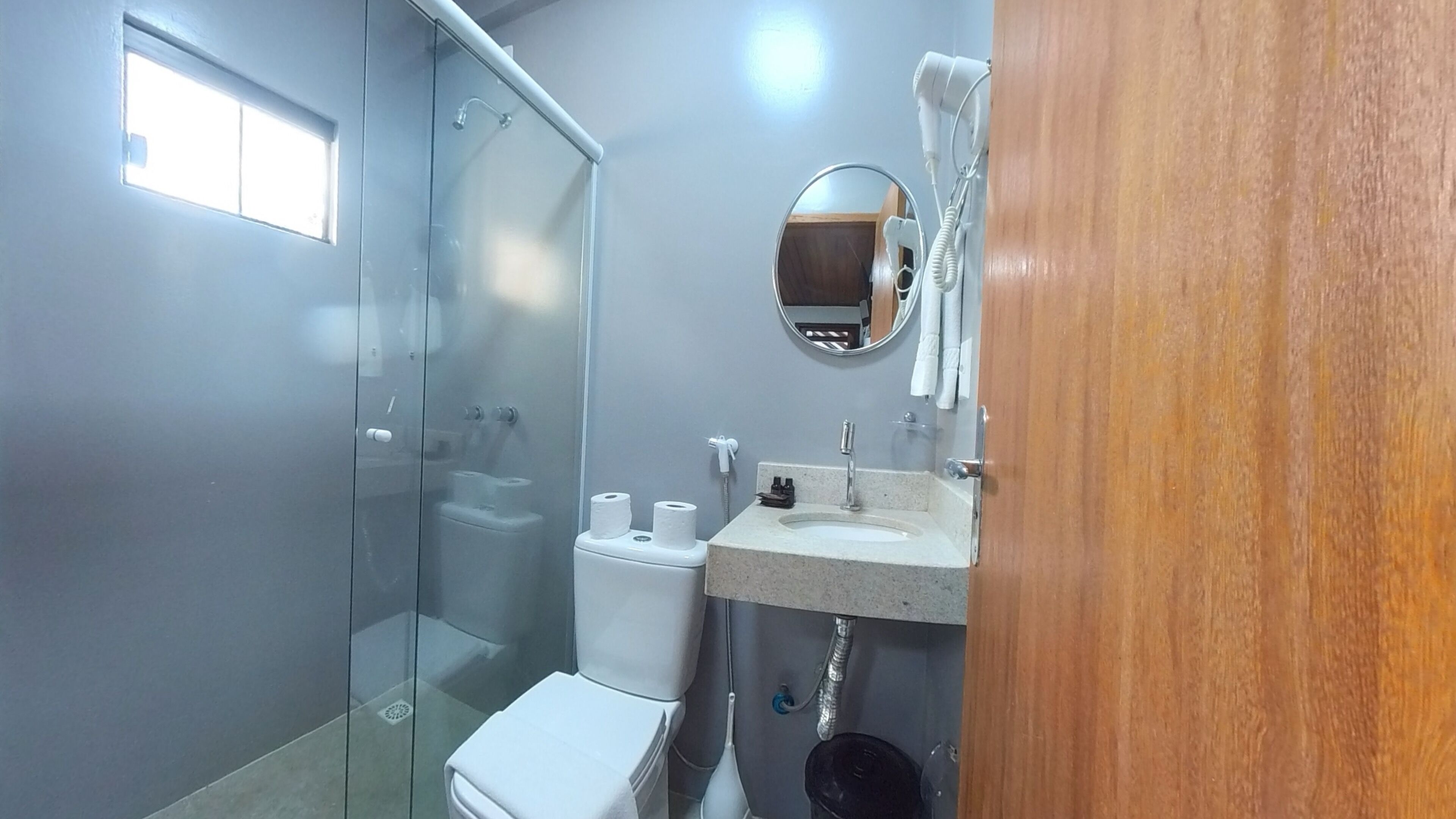 Un baño con cabina de ducha de vidrio, inodoro, lavabo con espejo y puerta de madera.