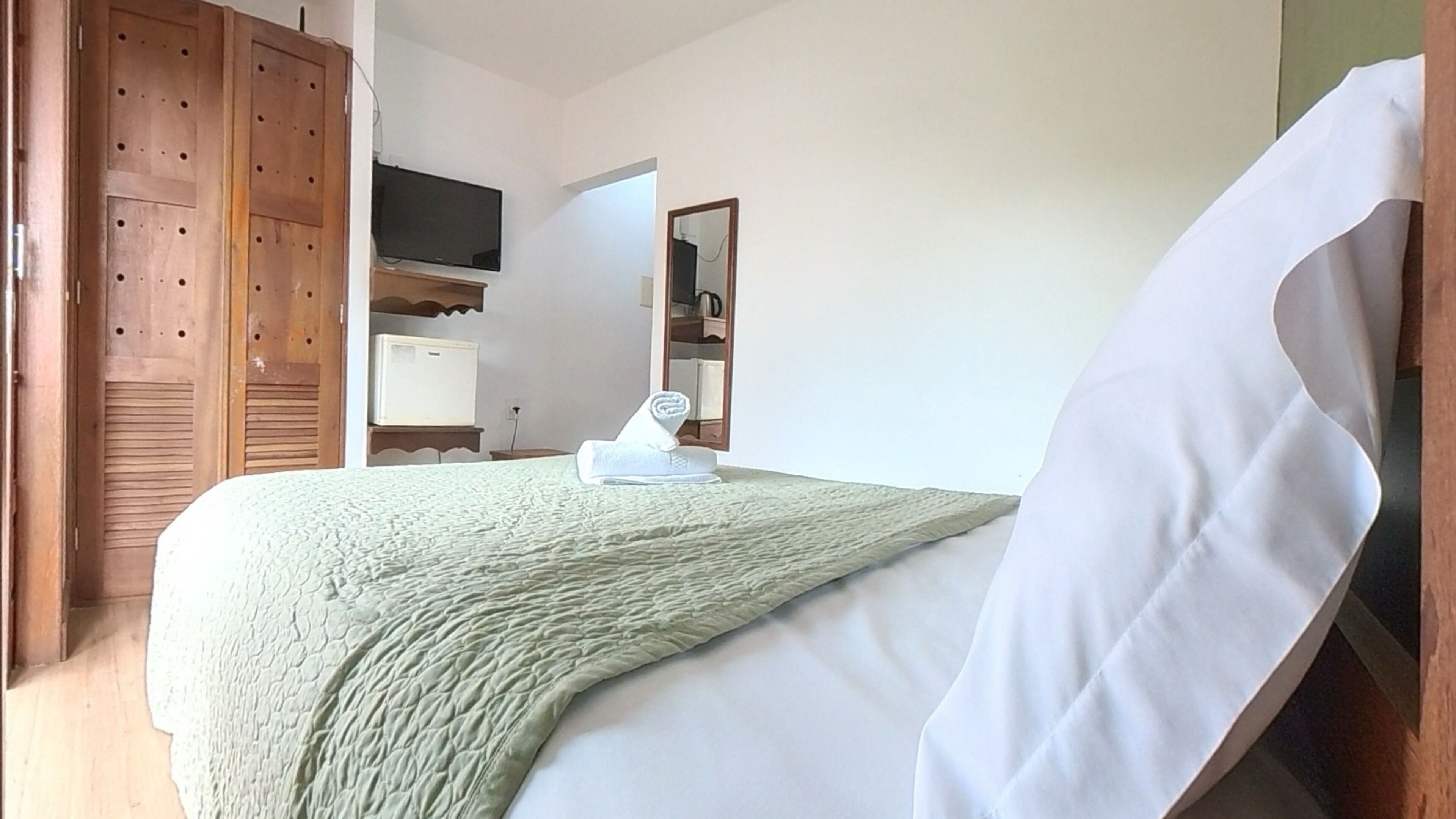 A bedroom with a bed, a TV, a mirror, and a wardrobe.