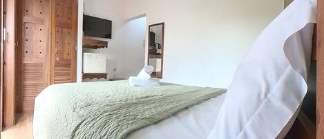 A bedroom with a bed, a TV, a mirror, and a wardrobe.