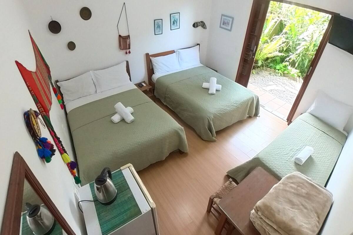 Ein Zimmer mit zwei Betten, einem kleinen Tisch mit Wasserkocher und Blick auf Grünfläche draußen.