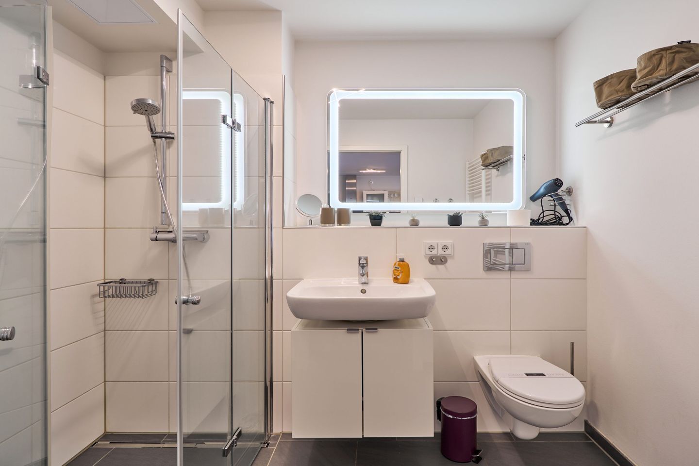 Un baño moderno con ducha envuelta en vidrio, un lavabo blanco, un espejo y un inodoro.