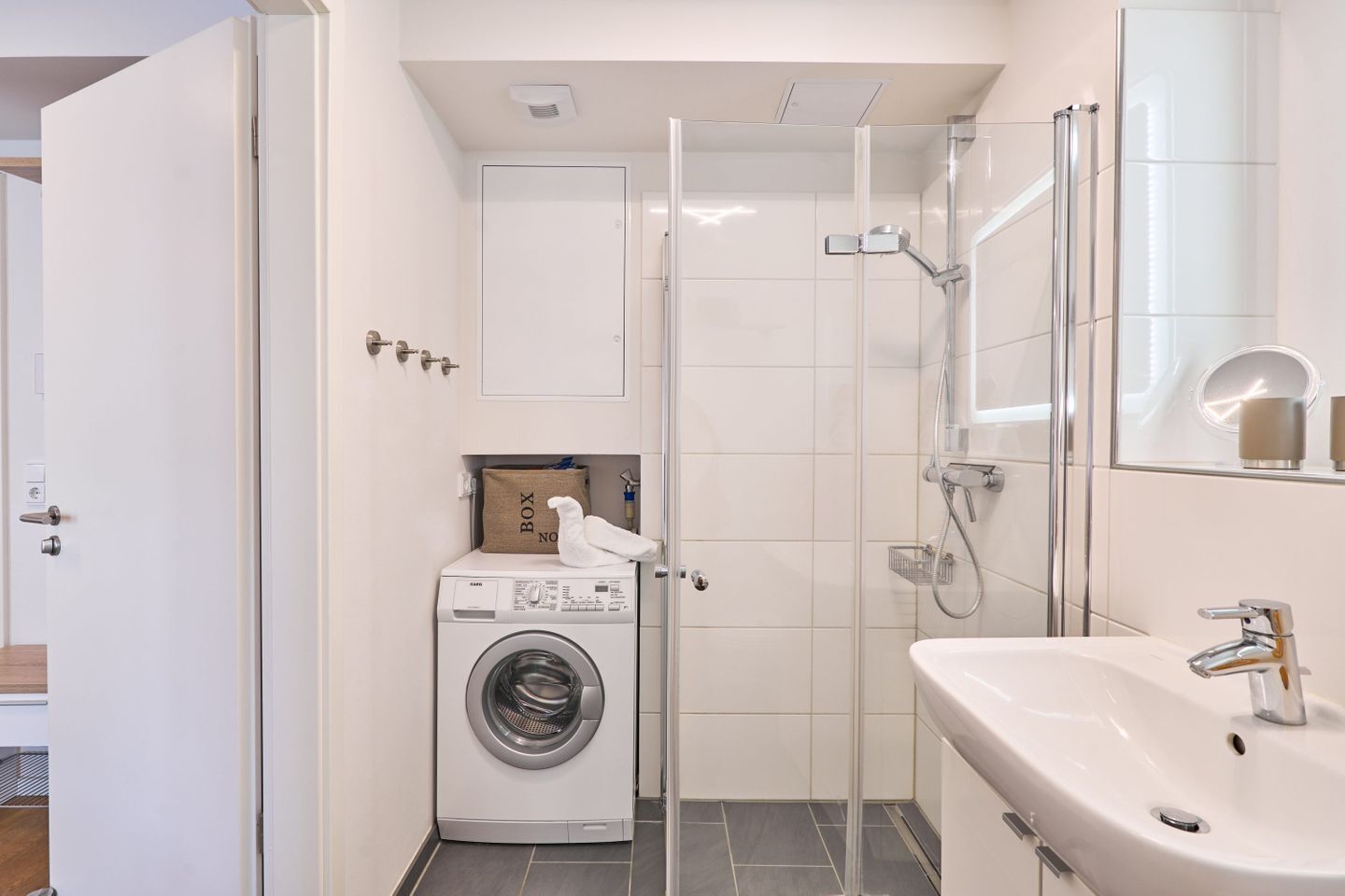A compact bathroom with a washing machine, a shower enclosure, and a sink.
