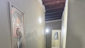 A hallway with a framed artwork on the left, a door with a handle, and a table with chairs on the right. - Sleeps 9 • 4 Queen Beds • Charming 2BR Apartment with AC & WiFi (Kingston)