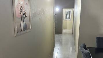 A hallway with a framed artwork on the left, a door with a handle, and a table with chairs on the right.