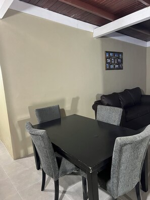 A dining area with a black table and grey chairs, a black sofa, and a framed photo collage on the wall. - Sleeps 9 • 4 Queen Beds • Charming 2BR Apartment with AC & WiFi (Kingston)