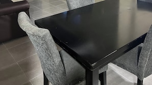 A dining area with a black table and four grey chairs, a television mounted on the wall, and a dark curtain on the left. - Sleeps 9 • 4 Queen Beds • Charming 2BR Apartment with AC & WiFi (Kingston)