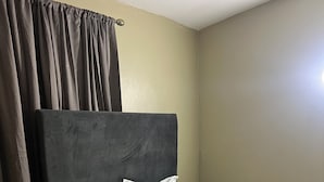 A single bed with a dark headboard and white bedding in a room with plain walls and a tiled floor. - Sleeps 9 • 4 Queen Beds • Charming 2BR Apartment with AC & WiFi (Kingston)