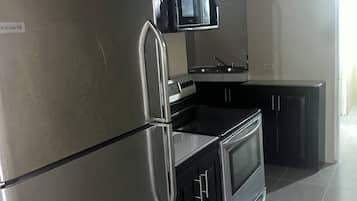 A modern kitchen with stainless steel appliances, black cabinets, and a tiled floor.