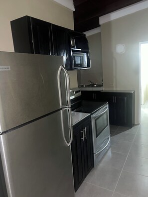 Una cocina moderna con electrodomésticos de acero inoxidable, armarios negros y suelo de baldosas.