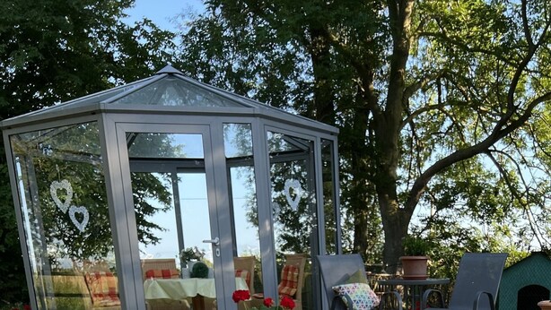 A glass greenhouse structure with a door, surrounded by outdoor furniture and potted plants. - Apartment 'Kuhstall' with Shared Terrace, Shared Garden and Wi-Fi (Werdum)