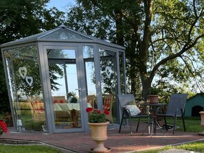 A glass greenhouse structure with a door, surrounded by outdoor furniture and potted plants. - Apartment 'Kuhstall' with Shared Terrace, Shared Garden and Wi-Fi (Werdum)