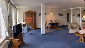 A living room with a television, a dining table with chairs, a cabinet, and a lamp. - Apartment 'Kuhstall' with Shared Terrace, Shared Garden and Wi-Fi (Werdum)
