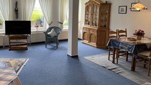 A living room with a television, a dining table with chairs, a cabinet, and a window with curtains. - Apartment 'Kuhstall' with Shared Terrace, Shared Garden and Wi-Fi (Werdum)