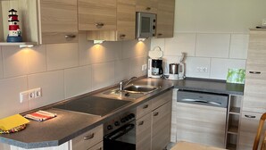 A modern kitchen with wooden cabinets, a built-in oven, a microwave, and a coffee maker. - Apartment 'Heuboden, 80qm' with Shared Terrace, Shared Garden and Wi-Fi (Werdum)