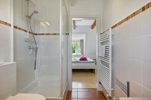 Een badkamer met douche en toilet, en een bed in de aangrenzende kamer.