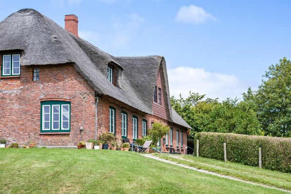 Een traditioneel bakstenen huis met rieten dak, een verzorgd gazon en een haag.