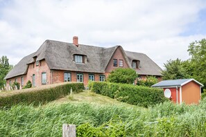 Een groot huis met rieten dak, bakstenen gevel en een klein rode tuinhuis.