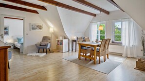 Un comedor con una mesa y sillas de madera, una estantería y un ventanal con cortinas.