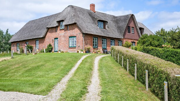 Una gran casa de ladrillo con techo de paja, camino de grava y césped bien cuidado.