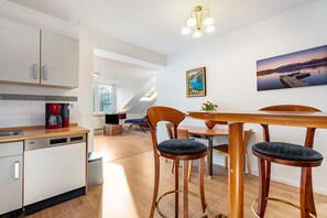 A modern kitchen with a dishwasher, a coffee maker, and a dining area with a wooden table and chairs.