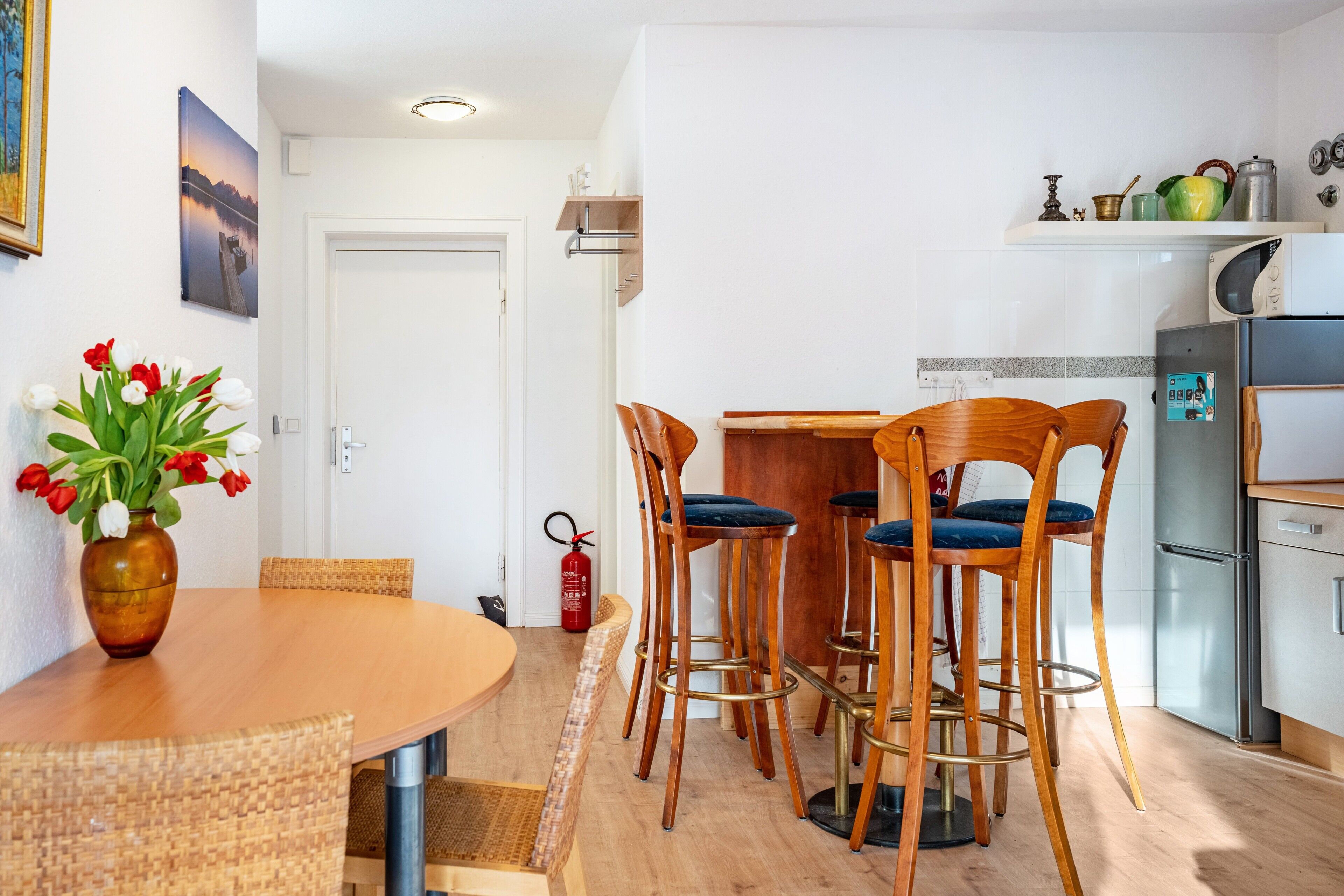 Una cocina moderna con comedor, sillas de madera, una mesa redonda y un jarrón con tulipanes rojos y blancos.