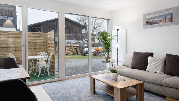 A modern living room with a sofa, a coffee table, and a dining area with chairs and a table. - Apartment 'König' with Mountain View, Shared Terrace and Wi-Fi (Lustenau)