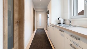 A narrow hallway with a wooden door, a white wall, a dark carpet, and a kitchen area with a sink and cabinets. - Apartment 'König' with Mountain View, Shared Terrace and Wi-Fi (Lustenau)